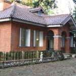 赤茶色のレンガ造りの大山別邸の外観、建物の間に低い柵が見える風景