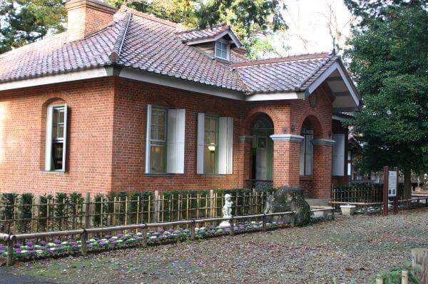 赤茶色のレンガ造りの大山別邸の外観、建物の間に低い柵が見える風景